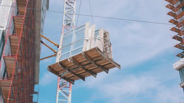 De kraan tilt dubbele beglazing op. Een kraan heft ramen op voor installatie in een woongebouw. Werken in de thuisbouw — Stockvideo