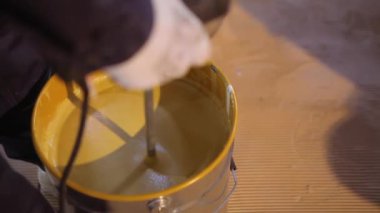 Kovada boya karıştırmak. Yakın plan sarı boya kovada karıştırılıyor.