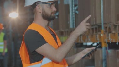 Büyük bir fabrikanın depo müdürü. Bir depoda elinde tablet olan bir müdür malları kontrol ediyor..