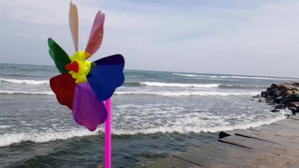 Moinho de vento infantil no mar. Um moinho de vento das crianças no vento, um moinho de vento colorido das crianças está girando do vento na costa. — Vídeo de Stock
