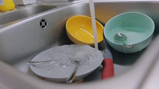 Platos sucios en el fregadero. Rutina en la cocina. El agua del grifo se vierte en platos sucios. Proceso de lavado de platos. Tareas — Vídeos de Stock