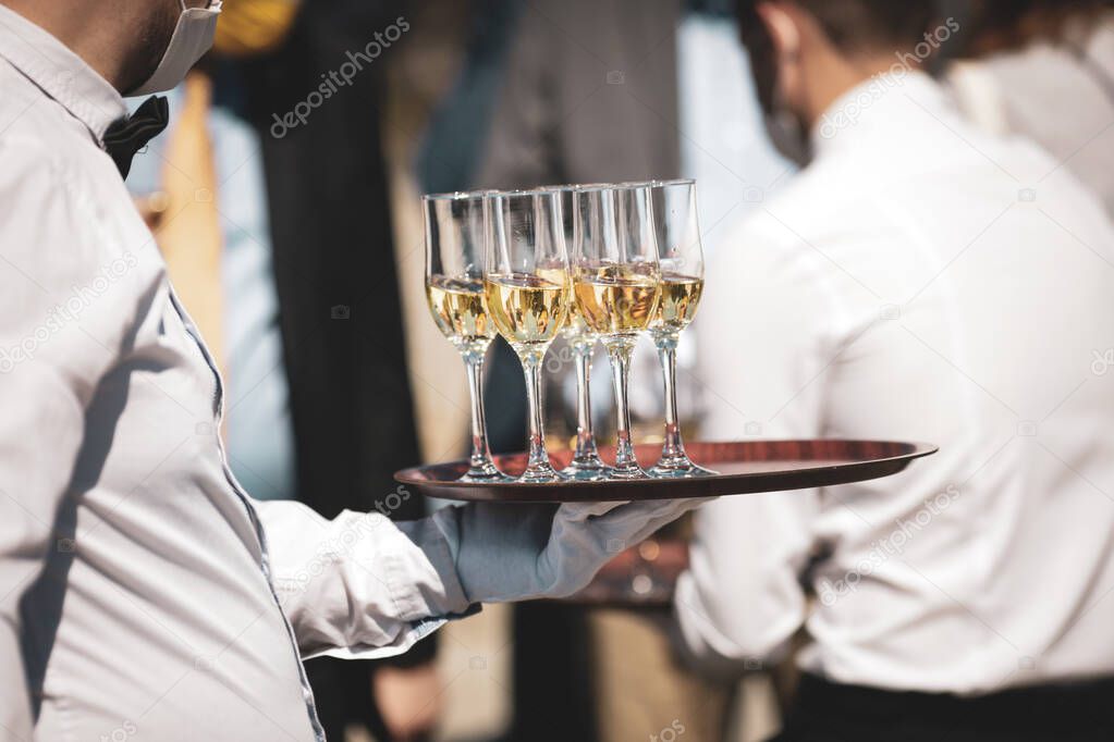 Shallow depth of field (selective focus) details with a waiter walking around and giving sparkling wine to the guests of an event.
