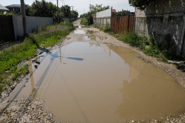Romanya 'nın Bükreş kentinde çamurlu bir yolda meydana gelen yağmur sonrasında su dolu dev çukurlarla sığ alan derinliği (seçici odak) ayrıntıları.