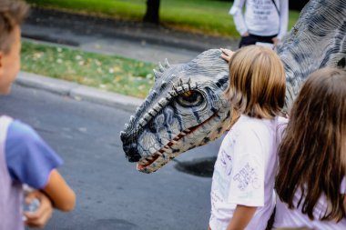 Bükreş, Romanya - 29 Ağustos 2021: İnsanlar arasında etobur dinozor kostümü giymiş bir adam, Bükreş 'te düzenlenen bir açık hava etkinliğinde kendisini okşamalarına izin veriyor.