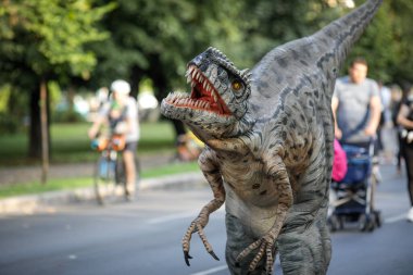 Bükreş, Romanya - 29 Ağustos 2021: İnsanlar arasında etobur dinozor kostümü giymiş bir adam, Bükreş 'te düzenlenen bir açık hava etkinliğinde kendisini okşamalarına izin veriyor.