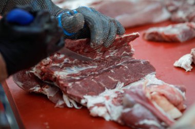 Bir kasap eliyle detaylar, birinde bıçak, diğerinde metal eldiven, domuz leşi kesme..