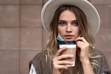 Karantina tecridi sona erdi. Aşılanmış kız koruyucu maskeyi çıkarırken kahve içiyor.