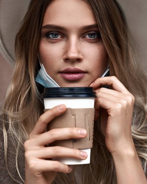 Karantina tecridi sona erdi. Aşılanmış kız koruyucu maskeyi çıkarırken kahve içiyor.