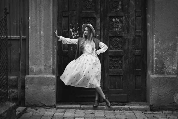 Joven modelo hermoso a la moda en sombrero en la ciudad vieja. Vestido blanco ondeando en el viento. Retrato en blanco y negro. — Foto de Stock