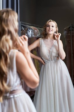 Parıltı ve pullarla süslenmiş gümüş sarısı, beyaz şifonlu balo elbisesi giyen genç ve güzel bir kız. Elbise kiralama servisinin soyunma odasında aynanın önünde manken..