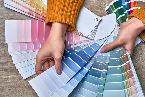 Color wheel for choosing paint tone. Hands of female interior designer working with palette for choosing colors. Creative process concept. Comparing options with matching hues.