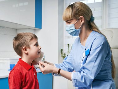 KBB 'deki kadın doktor muayeneden önce çocuk patentinden koruyucu yüz maskesi takıyor veya çıkarıyor.