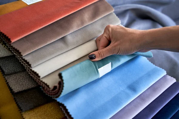 Choosing upholstery fabric color and texture from various colorful samples in a store. Female customer hands touching textile. — Stock Fotó