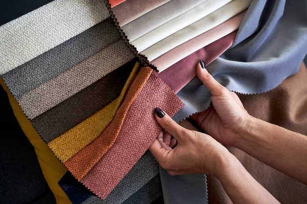 Choosing upholstery fabric color and texture from various colorful samples in a store. Female customer hands touching textile.