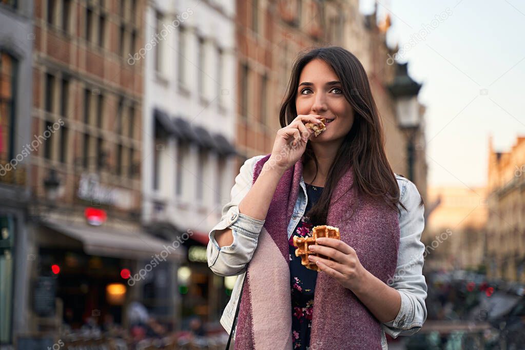 Happy girl walk and eat Belgian waffles on city street