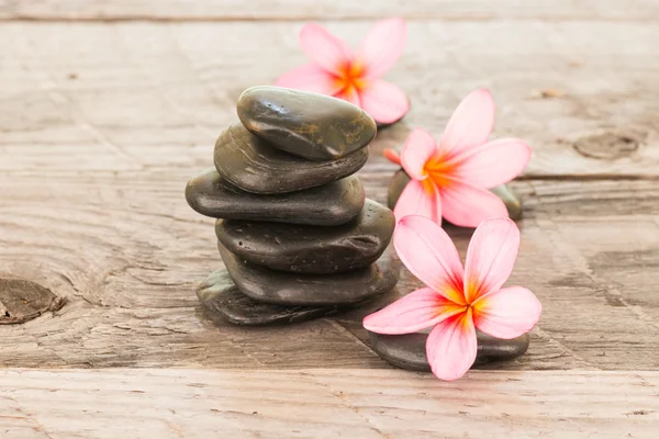 Plumeria Blumen und schwarze Steine auf verwittertem Holzhintergrund — Stockfoto