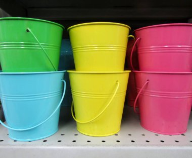 Deponun rafında parlak renkli kaplanmış galvanizli kovalar.
