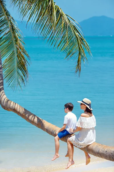 Moeder en zoontje op tropisch strand zittend op palmboom — Stockfoto