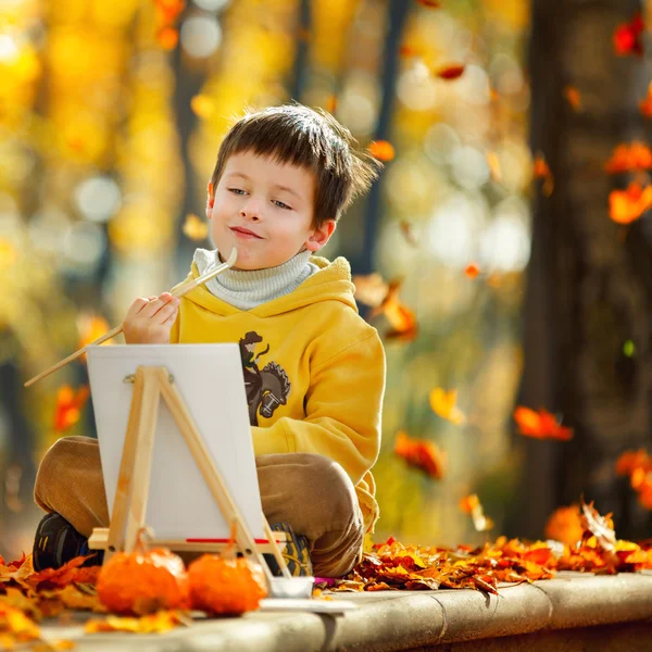 Симпатичный маленький мальчик рисует в золотом осеннем парке — стоковое фото