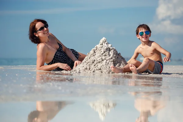 Joven madre y su pequeño hijo construyendo castillo de arena en la playa — Foto de Stock