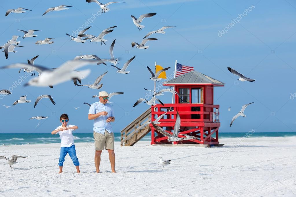 Father and his son feeding seagulls on tropical beach