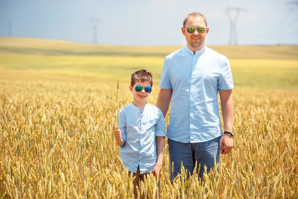 Padre feliz con hijo pequeño caminando felizmente en el campo de trigo — Foto de Stock