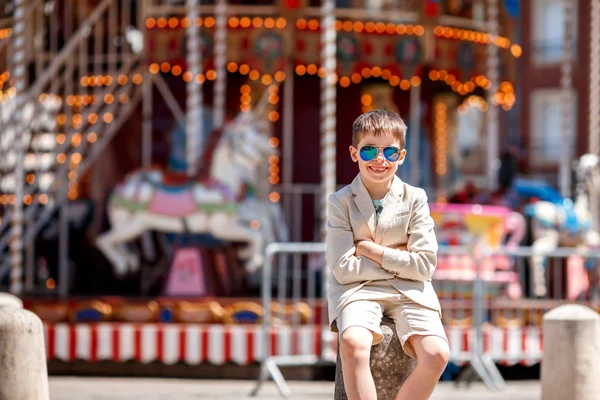 Niño con estilo en un bonito traje y gafas cerca del tradicional tiovivo francés — Foto de Stock