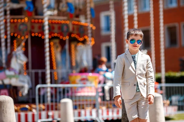 Stijlvolle jongen in een mooi pak en glazen in de buurt van de traditionele Franse merry-go-round — Stockfoto