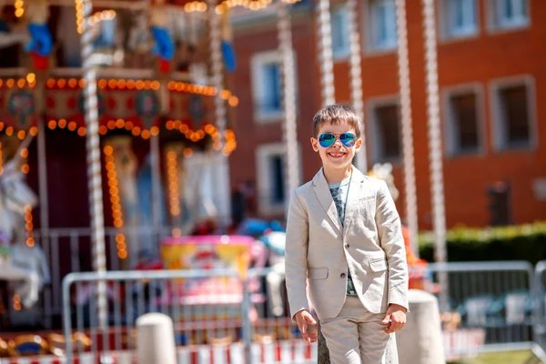 Criança elegante em um terno agradável e óculos perto do tradicional francês alegre-go-round — Fotografia de Stock