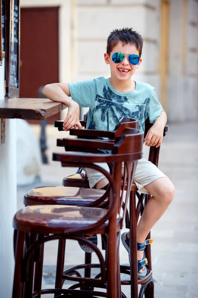 Cute little boy sitting on a chair in outdoor cafe — Stock Photo, Image