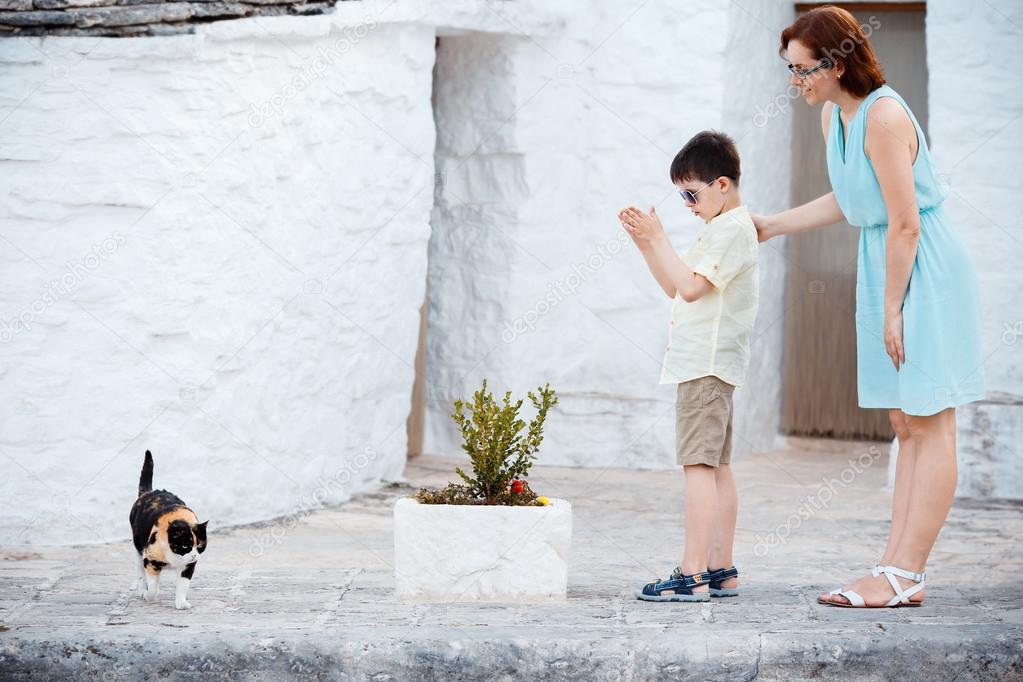 Mother and son met a cat while walking narrow streets ot typical italian town