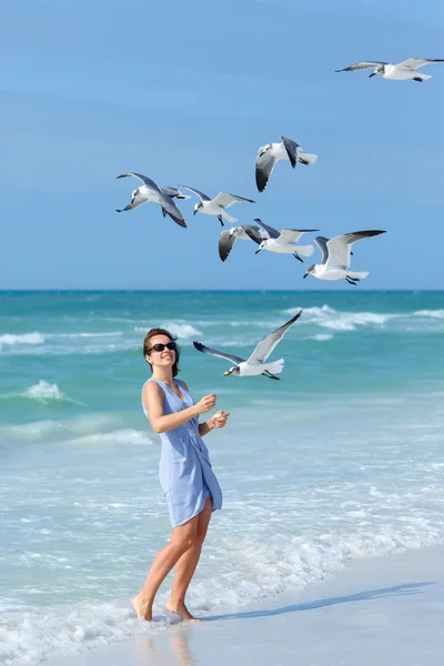 Young woman feeding seagulls on tropical beach — Stock Photo, Image