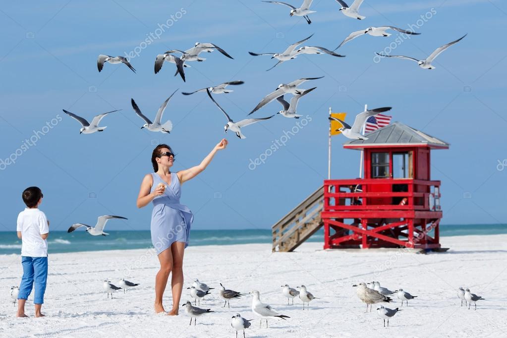 Young mother and her little son feeding seagulls on tropical beach
