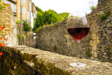 Close-up of a half-empty glass of red wine on the stone wall of the Oldest pub in Dover. Building dates to 1365. Famous as a Channel swimmers pub. clipart