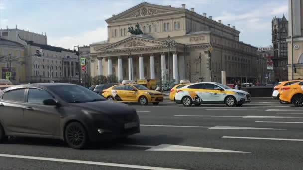 Moskva: Biltrafikk på Teatralnij oppkjørsel, Bolsjojteateret på bakgrunn. Gul Yandex drosjebil. – stockvideo