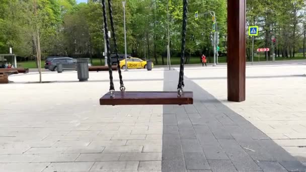 Moscow: Unoccupied swing swinging, vacant seat, street traffic on background, Uber yellow taxi waiting on the traffic light in the backdrop. Street cleaning workers. 4K video 3840x2160 — Stock Video