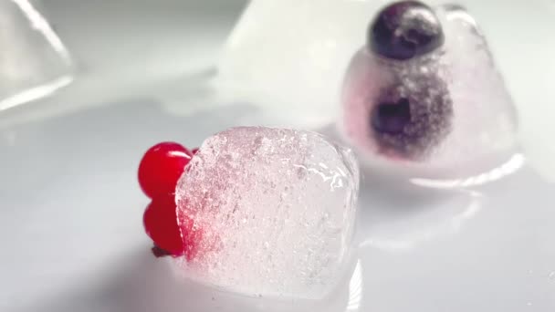 Kostka ledu se točí dokola. Detailní záběr kusy ledu se zmrazenými bobulemi uvnitř na bílém pozadí. Tající ovocný led. 4K video 3840x2160 — Stock video