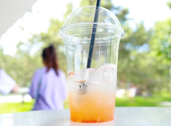 Rest of refreshing drink in a plastic disposable frosty cup, heat wave in the city. Orange juice with ice in glass. Abandoned cold drink on an outdoor cafe table. Half empty plastic cup. Hot weather