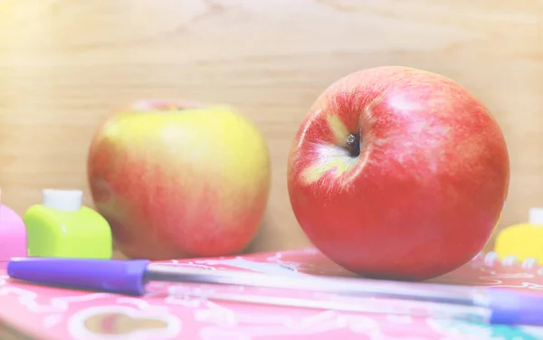 Selective focus of two apples on wooden background surrounded with school supplies. School theme concept. School lunch. Apple a day