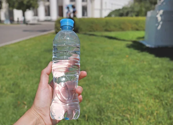夏日阳光明媚 绿油油的自然背景下 手中拿着一瓶纯净水 在炎热的天气里口渴 中暑风险概念 图库照片