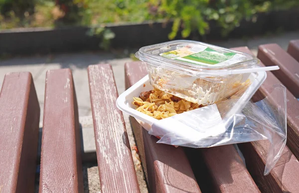 Leftovers food in disposable plastic package. Food left on a bench in plastic lunch boxes. Fast food. Lunch outdoor on a summer day. Plastic waste, plastic pollution. Consumerism. Food consuming.