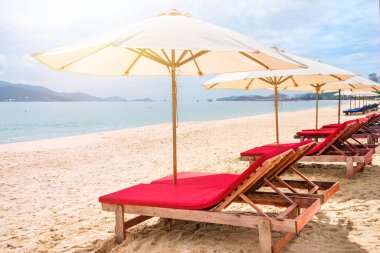 Boş deniz sahilinde kırmızı şilteli ve şemsiyeli sıra sıra iskemleler. Boş bir plajda güneşli bir gün. Vietnam, Nha Trang
