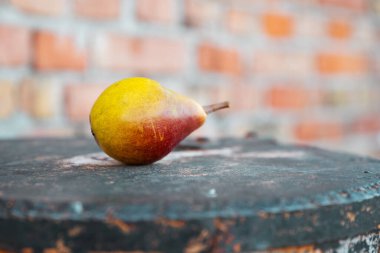 Sarı olgun armut, paslı metal bir fıçının üzerinde, kırmızı tuğla bir duvarın arka planında yatıyor.