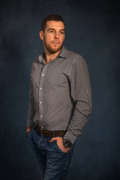 Портрет молодого красивого мужчины в клетчатой рубашке и джинсах, стоящих на темном фоне — стоковое фото