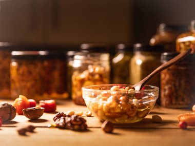 Çiftçi Bal fındıkla karıştırılmış, şeffaf bir tabakta tohumlar, tahta kaşık, ceviz, kayısı, sade ahşap mutfak masasında kurutulmuş kayısı. natürmort