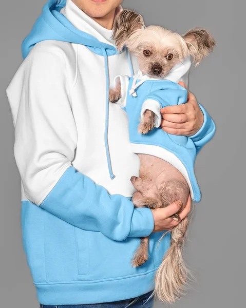 Um jovem tem um cão chinês deitado nos braços. Ambos usam as mesmas roupas. — Fotografia de Stock