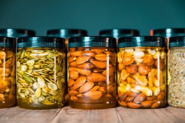 Fındık, tohum ve kurutulmuş meyvelerle karıştırılmış bal. Şeffaf kavanozlarda bal, çizgi halinde kapaklar ya da ahşap masada sıralar. Lezzetli sağlıklı yemek.