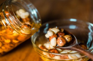 Çiftçi Bal fındık ile karıştırılmış, şeffaf bir kavanozdan dökülen tohumlar mutfak ahşap masada cam bir kaşık üzerinde ahşap bir kaşık. Hayat yakın çekim fotoğrafçılığı