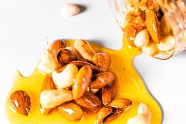 Siyah arka planda beyaz masaya dökülen fındıkla karıştırılmış bal kavanozu..