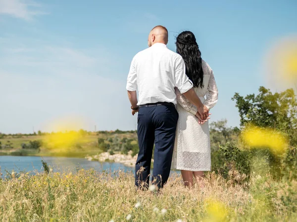 Genç, mutlu bir düğün çifti kameraya sarılıyor ve güneşli yaz gününde ufuk çizgisine bakıyor..
